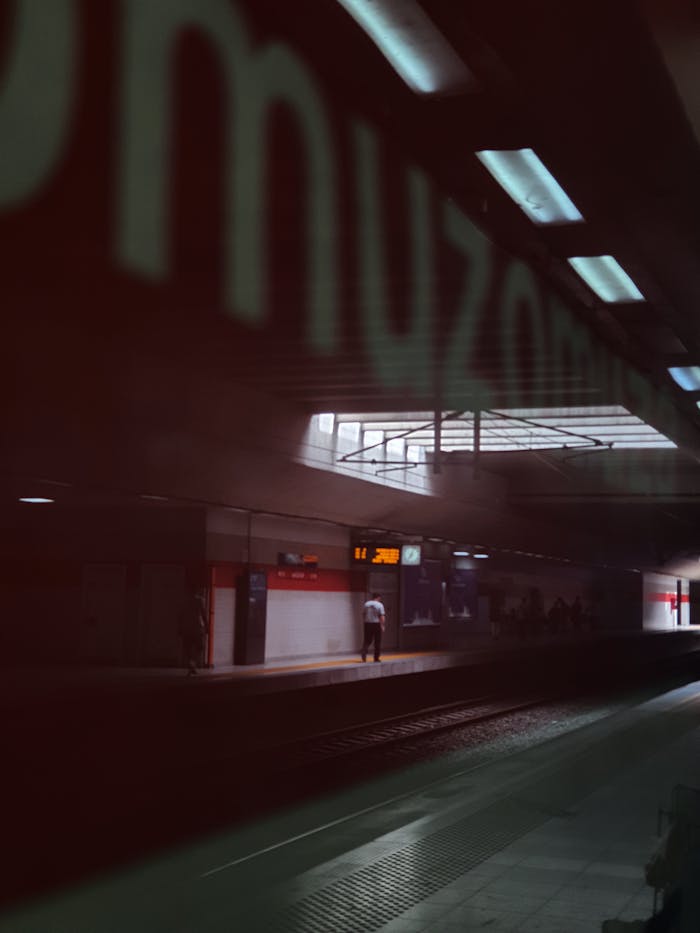 Dimly lit train station platform at night with passengers waiting, reflecting a moody urban atmosphere.